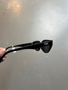 Detail-Produktbild von schwarzer Fendi Cat-Eye Sonnenbrille vor grauem Hintergrund.