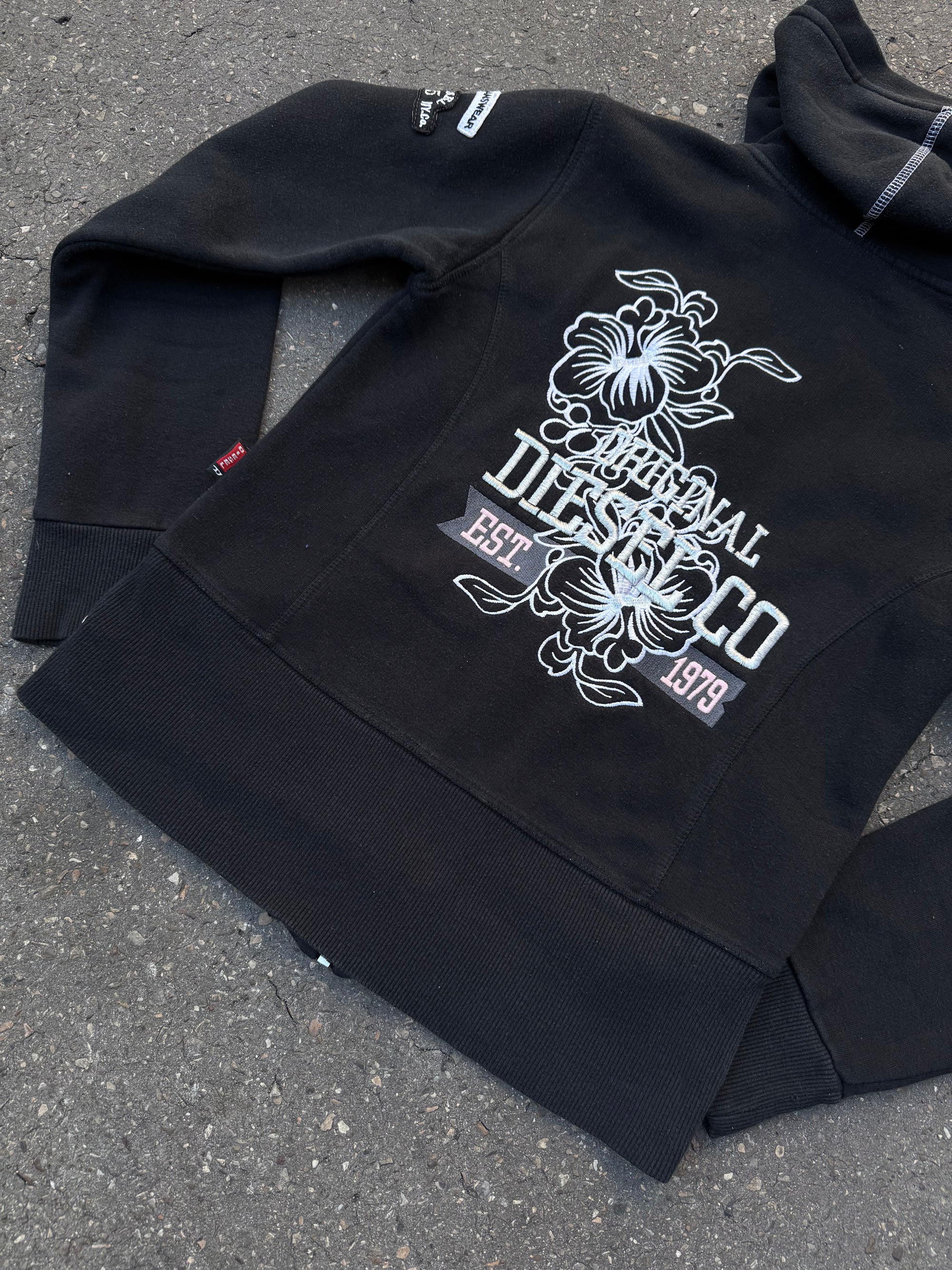 Ein schwarzer Zip Up Hoodie von Diesel mit dem Logo in weiß auf der Vorderseite und einem weißen Print auf der Rückseite