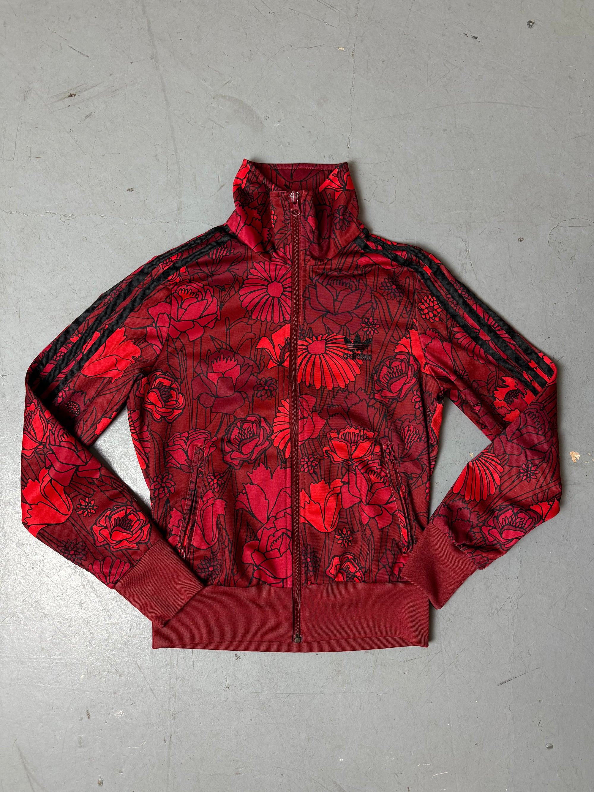 Rote Adidas Jacke mit Blumenmuster von Oben auf grauem Hintergrund
