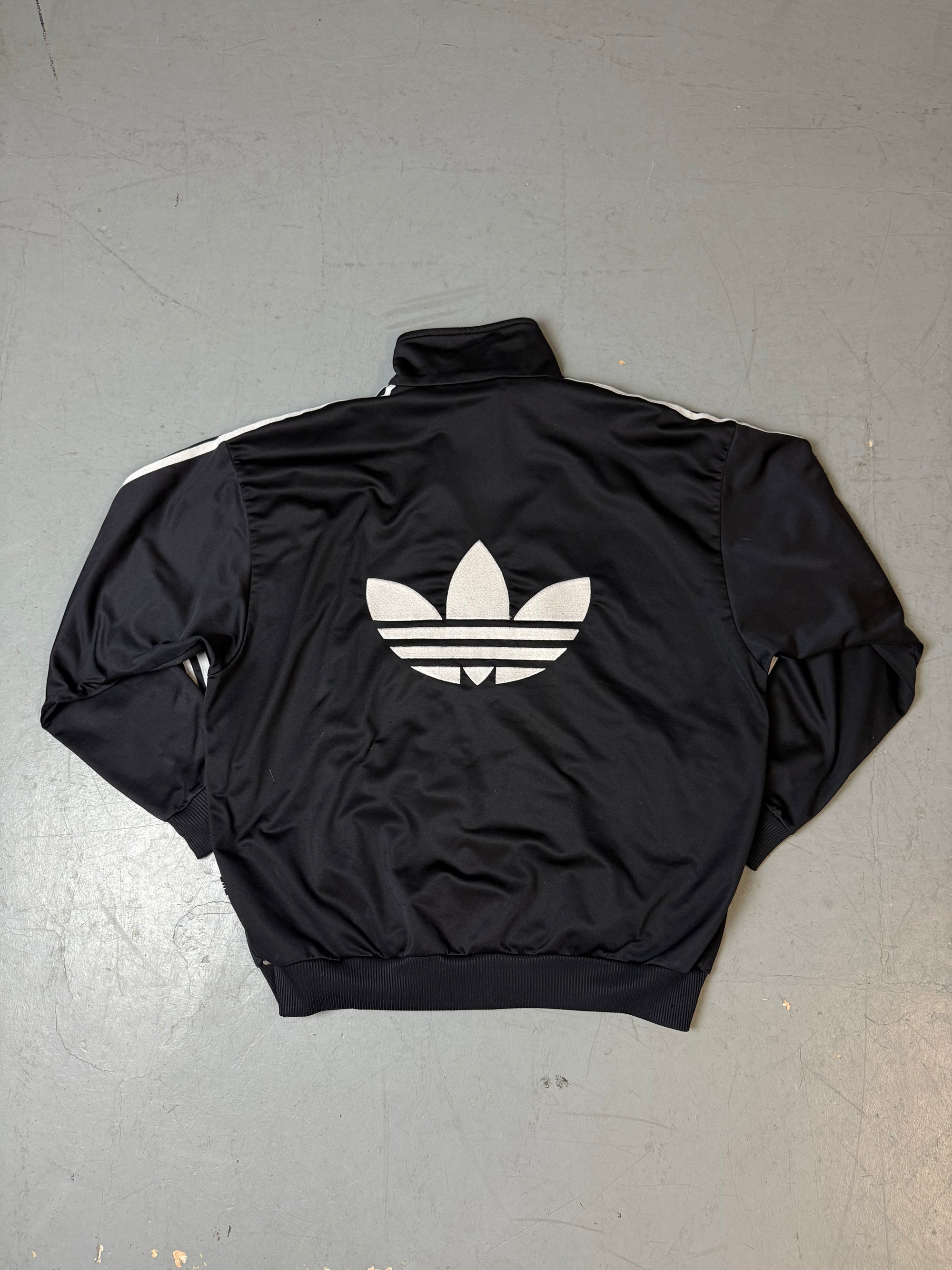 Eine schwarze vintage Adidas Track Jacke mit weißen Streifen und Firebird Logo 