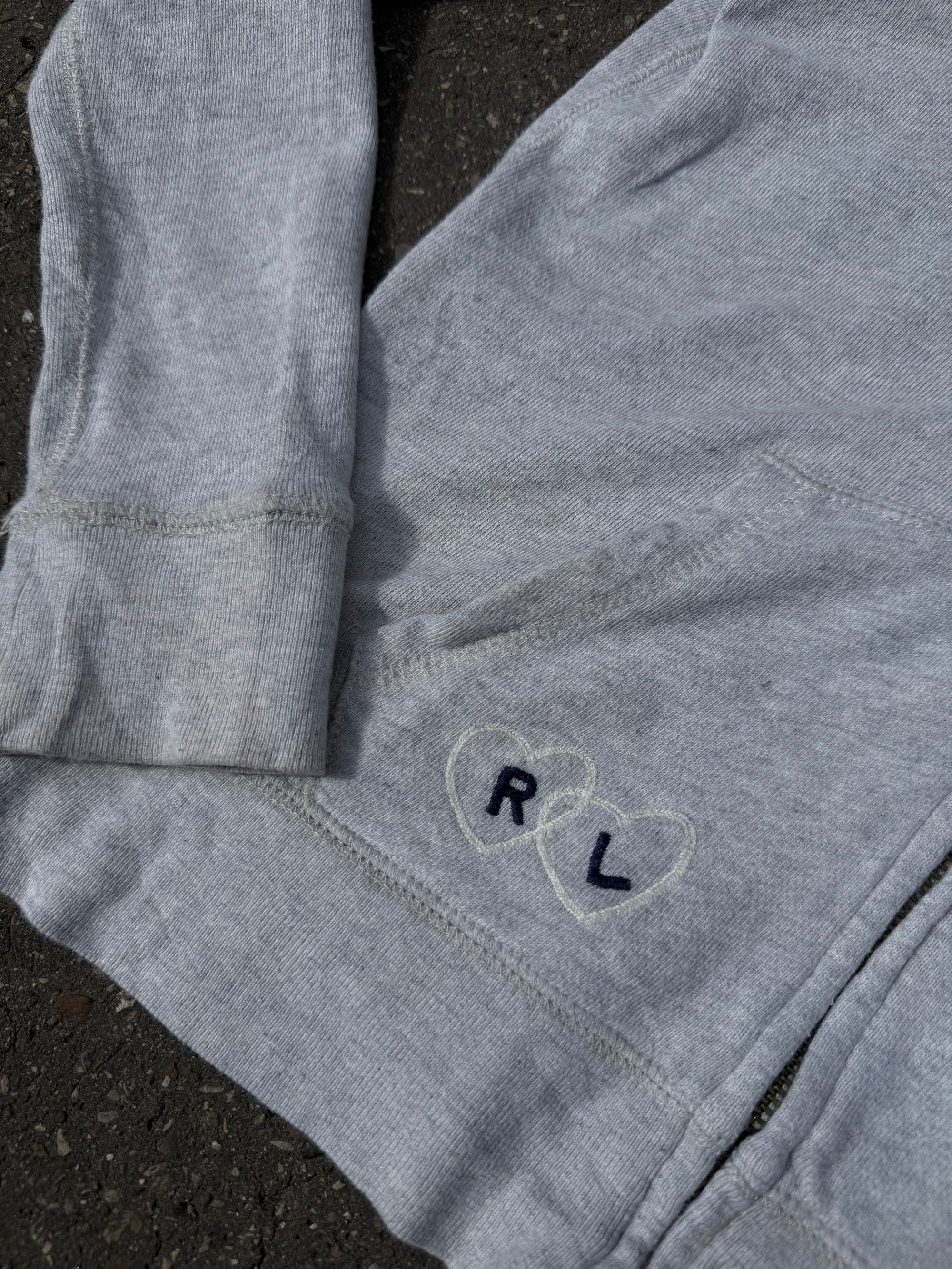 Ein grauer Zip Up Hoodie von Polo Ralph Lauren mit rosa Polo Aufdruck auf der Brust und kleinen patches überall verteilt in XS