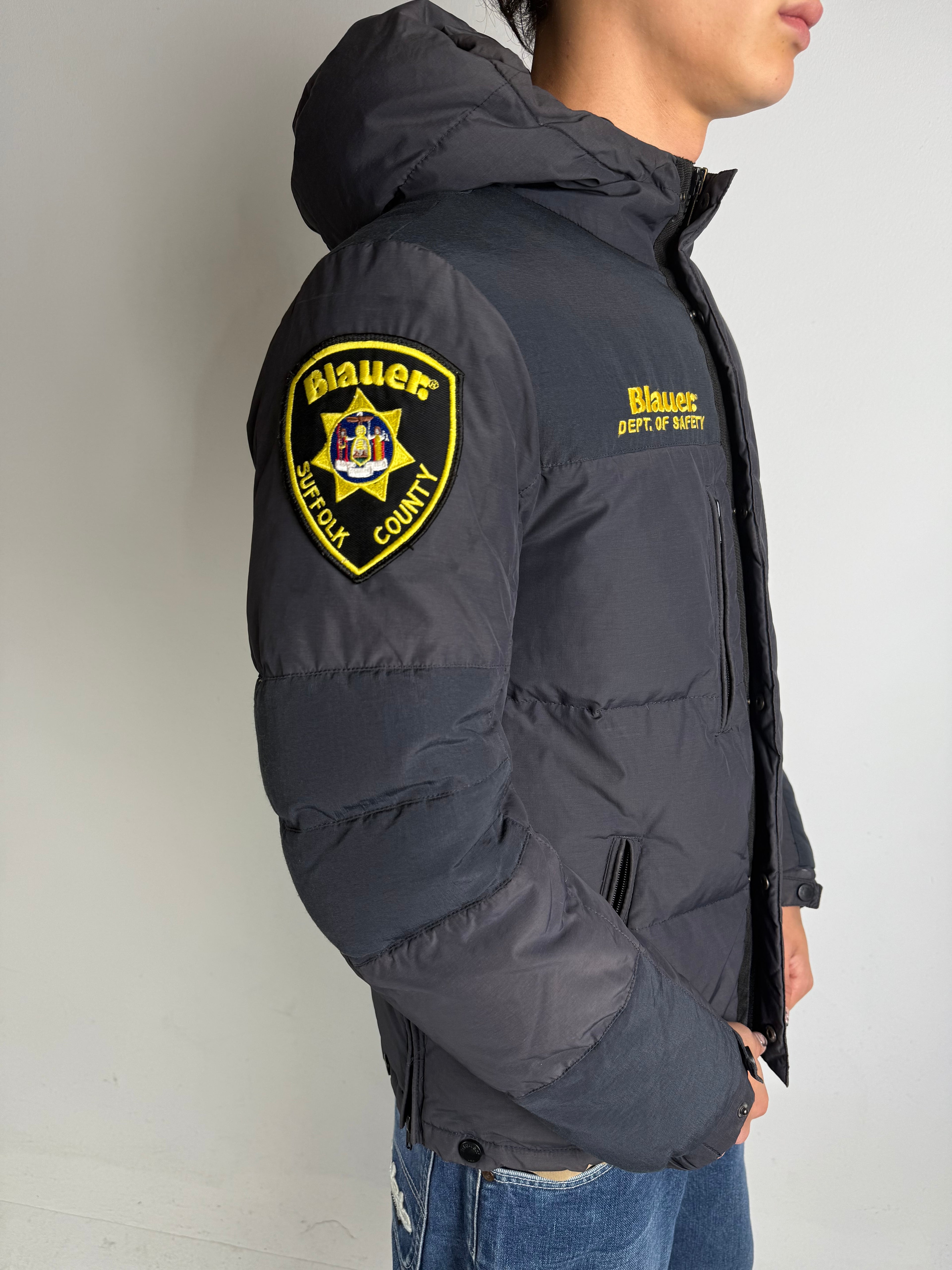 Detailliertes tragebild von Grauer Blauer Daunen Jacke in L vor grauer Wand