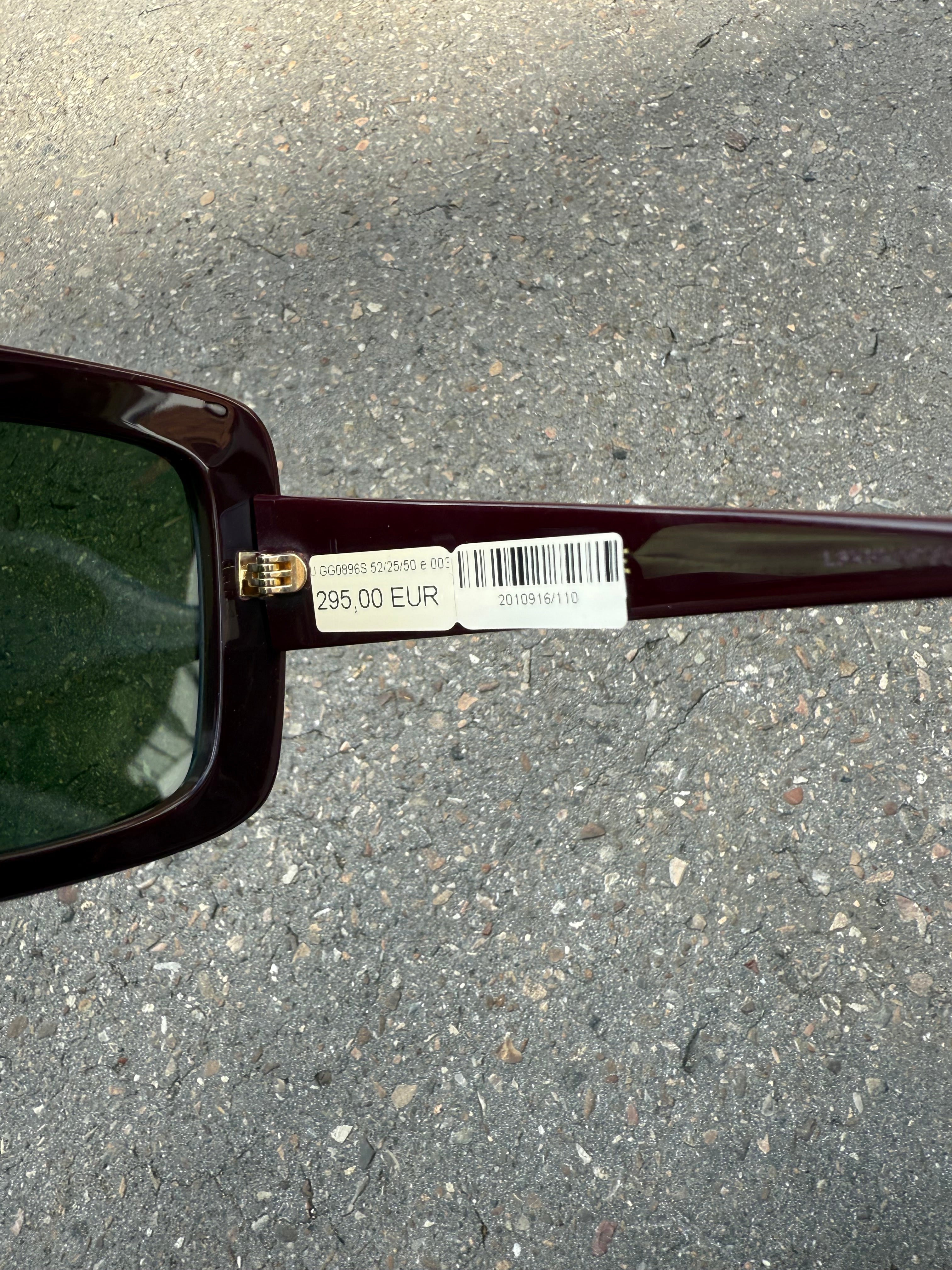 Eine burgunderrote Sonnenbrille von Gucci mit dem Logo in Gold an der Seite und großen quadratischen Gläsern