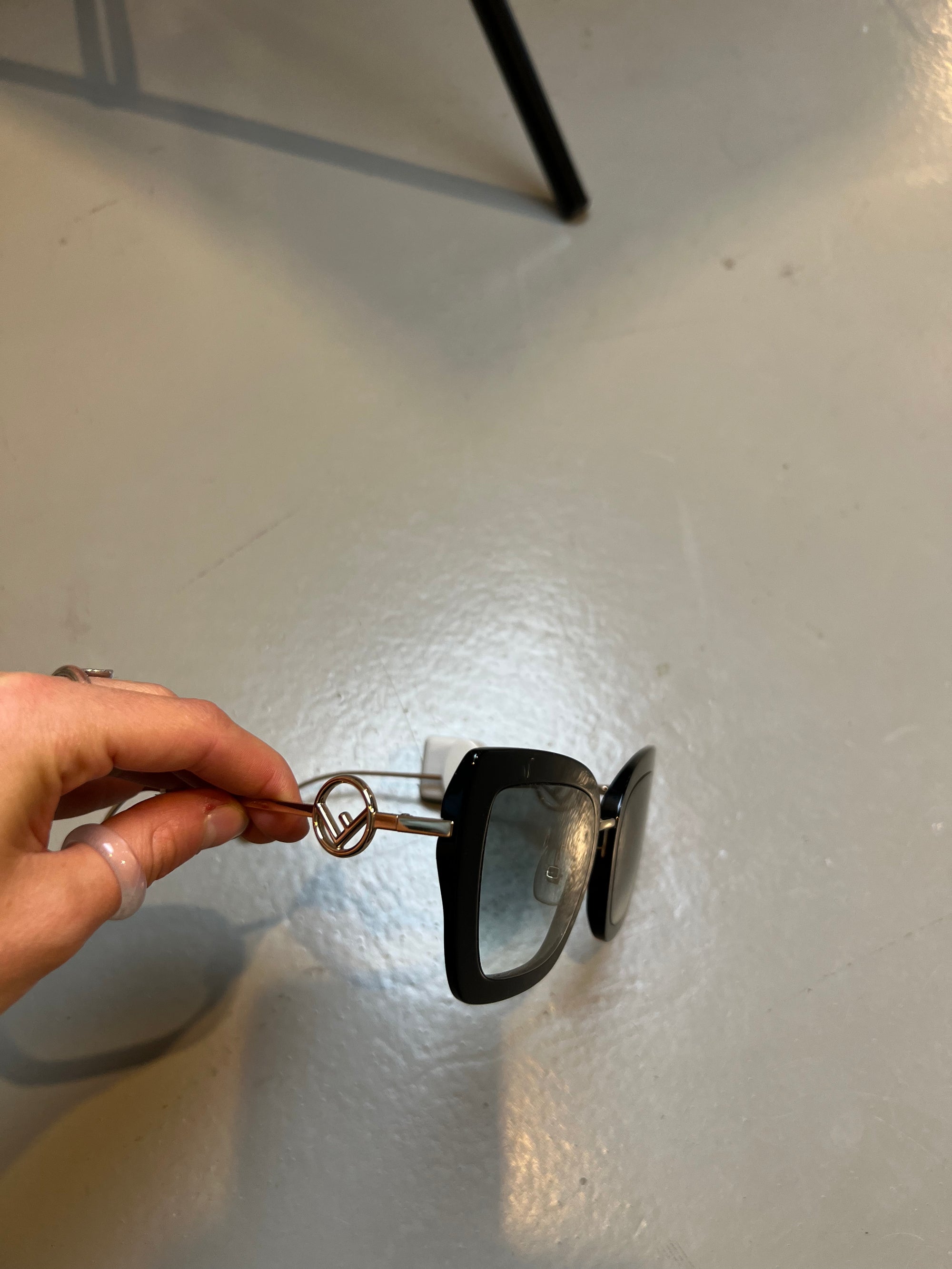 Detail-Produktbild von einer schwarzen Fendi Sonnenbrille auf grauem Boden.