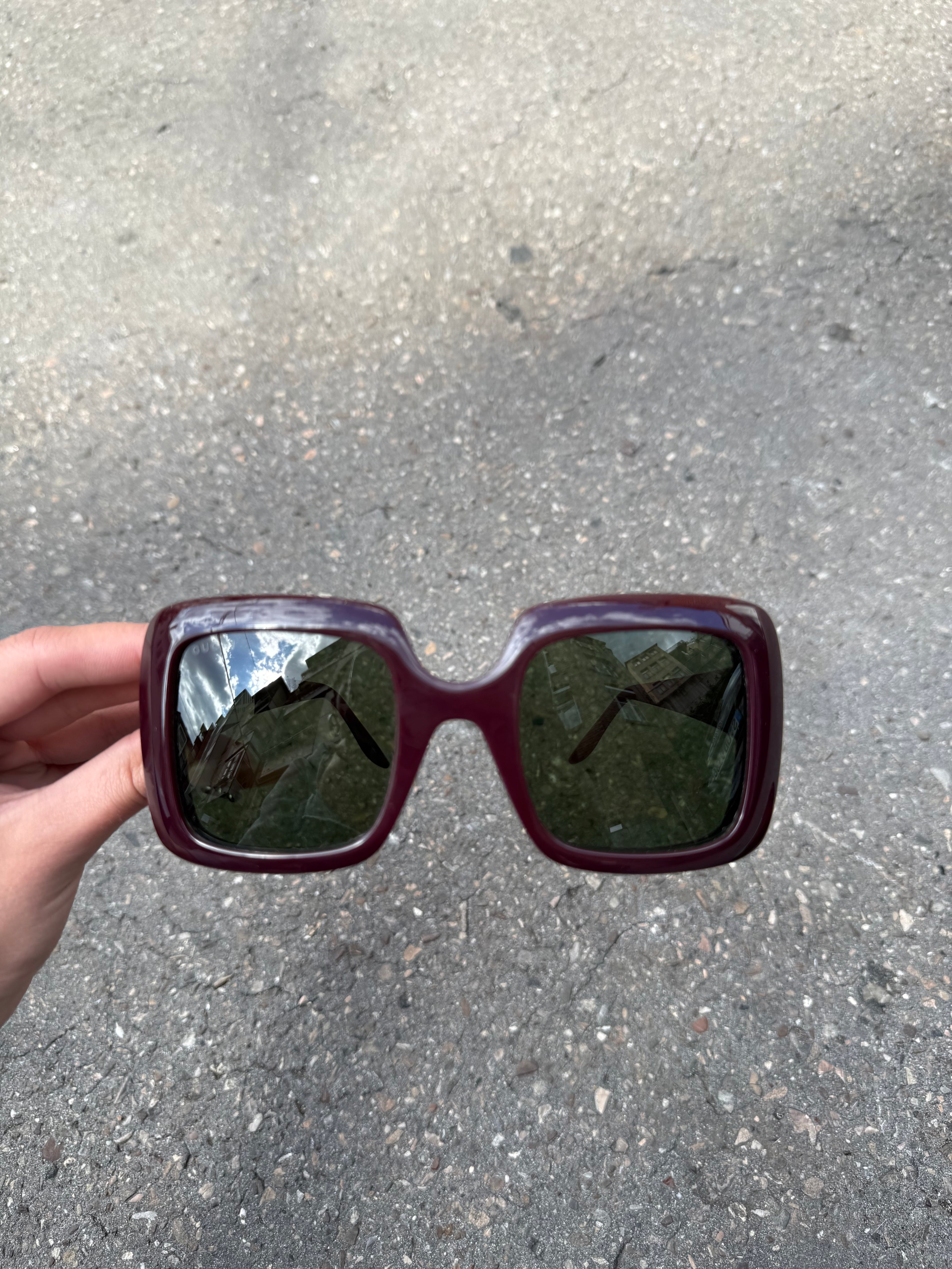 Eine burgunderrote Sonnenbrille von Gucci mit dem Logo in Gold an der Seite und großen quadratischen Gläsern