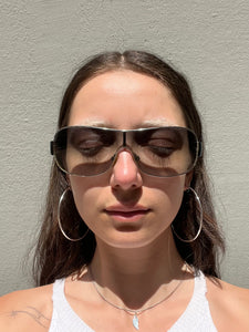 Weibliches Model trägt Dolce&Gabbana Sonnenbrillle mit schwarzem Bügel und 2000er Stil vor grauer Wand.