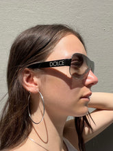Laden Sie das Bild in den Galerie-Viewer, Weibliches Model trägt Dolce&amp;Gabbana Sonnenbrillle mit schwarzem Bügel und 2000er Stil vor grauer Wand.