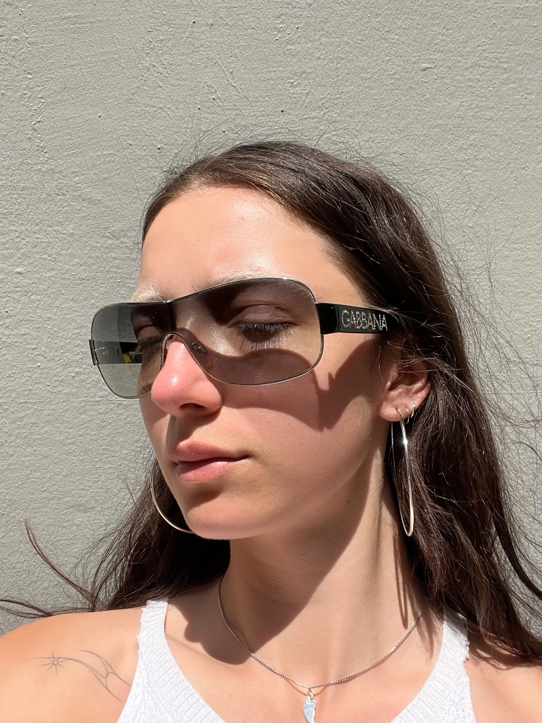 Weibliches Model trägt Dolce&Gabbana Sonnenbrillle mit schwarzem Bügel und 2000er Stil vor grauer Wand.