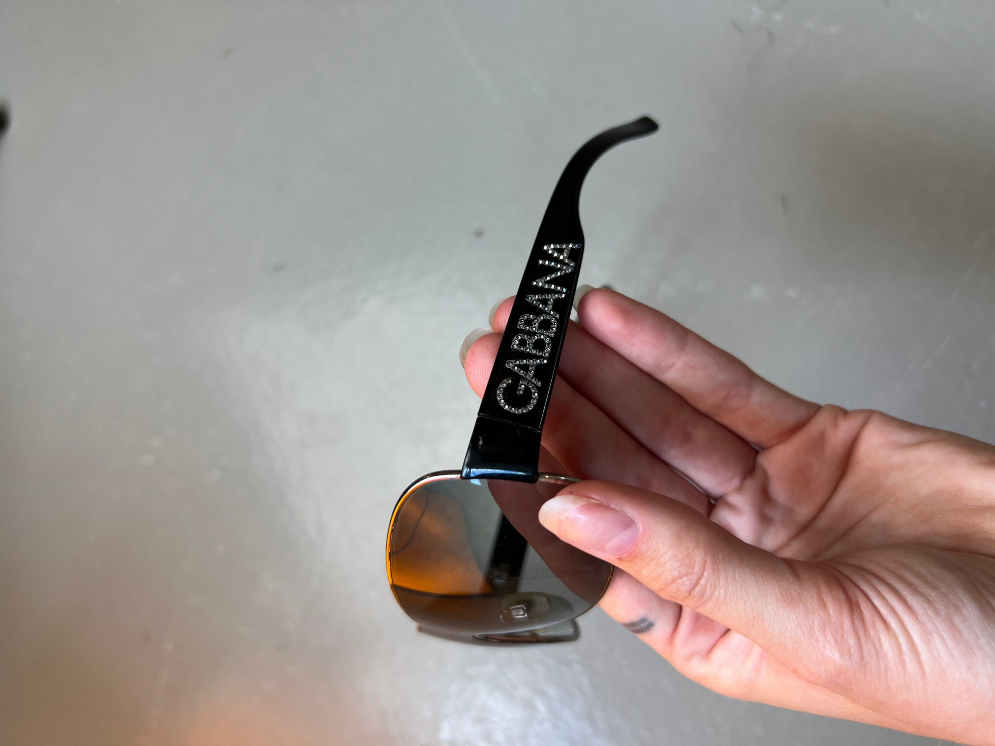 Produktbild von Dolce&Gabbana Sonnenbrillle mit schwarzem Bügel und 2000er Stil auf grauem Boden.