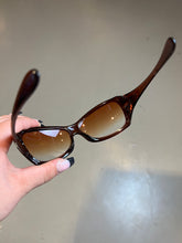 Laden Sie das Bild in den Galerie-Viewer, Produktbild von einer Braunen Oakley Sonnenbrille vor einer Grauen Wand