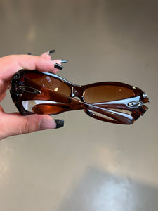 Produktbild von einer Braunen Oakley Sonnenbrille vor einer Grauen Wand