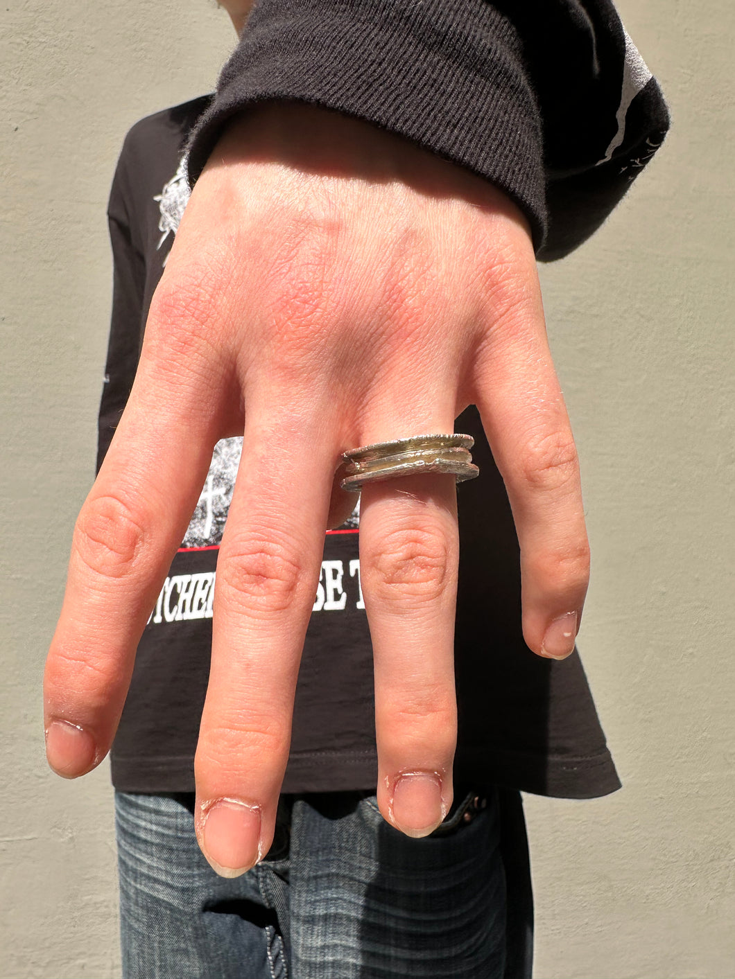 Tragebild vom Ringfinger von Ringsbyclausen Ring „Krater 3“ vor grauer Wand 