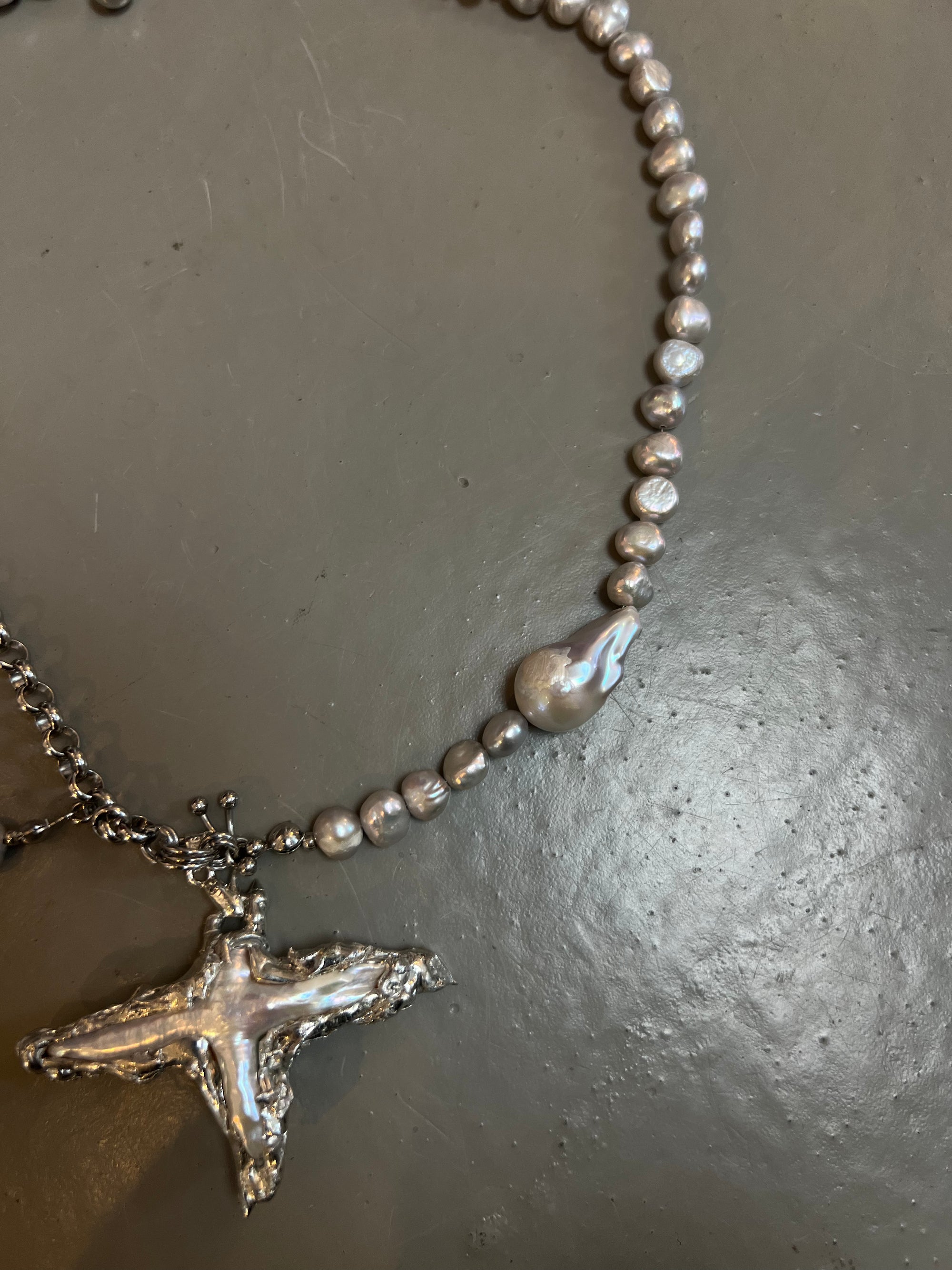 Detailliertes Produktbild von Xullery Cross Grey Pearl Necklace auf grauem Boden.