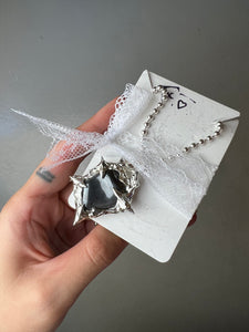 Produktbild von einer silbernen Halskette mit einem schwarzen Hematite Anhänger von Xullery vor einem grauen Hintergrund.
