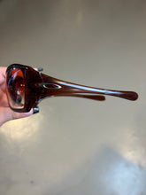 Laden Sie das Bild in den Galerie-Viewer, Produktbild von einer Braunen Oakley Sonnenbrillevon der Seite vor einer Grauen Wand