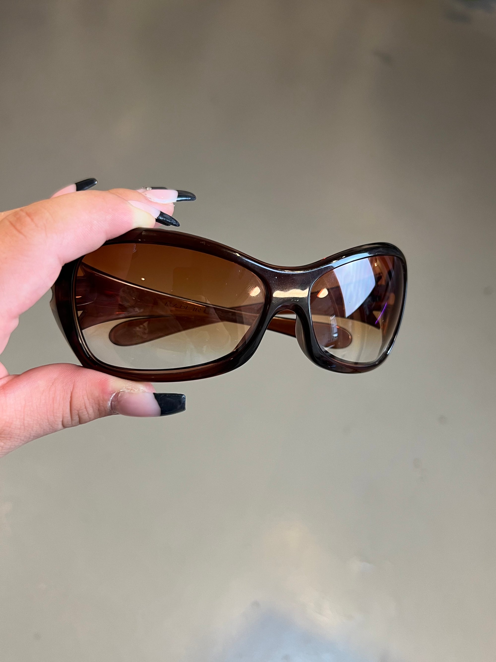 Produktbild von einer Braunen Oakley Sonnenbrille vor einer Grauen Wand