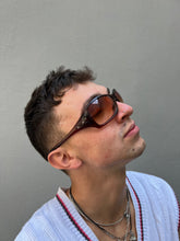Laden Sie das Bild in den Galerie-Viewer, Tragebild von einer Braunen Oakley Sonnenbrillevon der Seite vor einer Grauen Wand