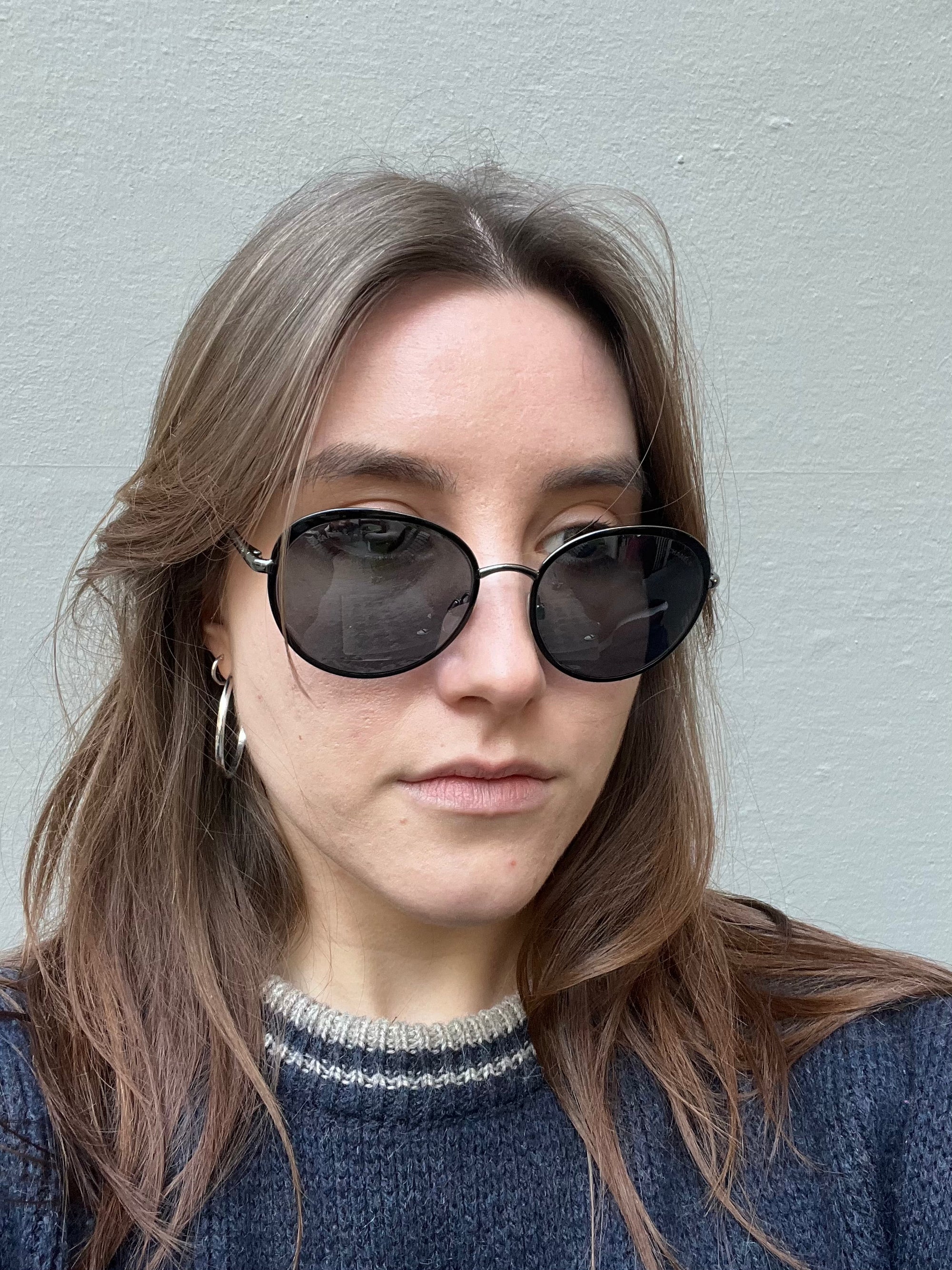 Tragebild einer runden Chanel Sonnenbrille in schwarz vor grauem Hintergrund.