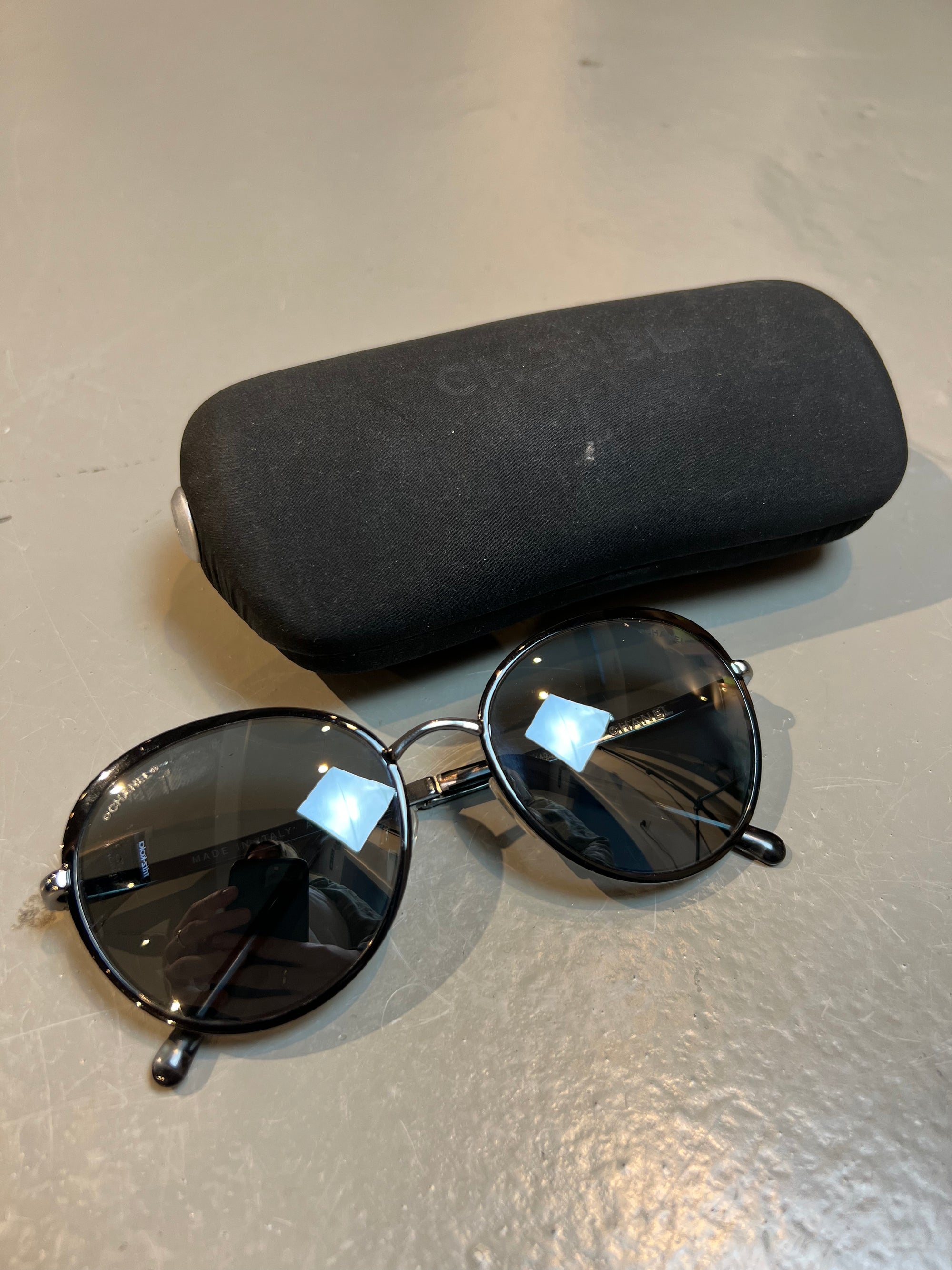 Produktbild einer runden Chanel Sonnenbrille in schwarz vor grauem Hintergrund.