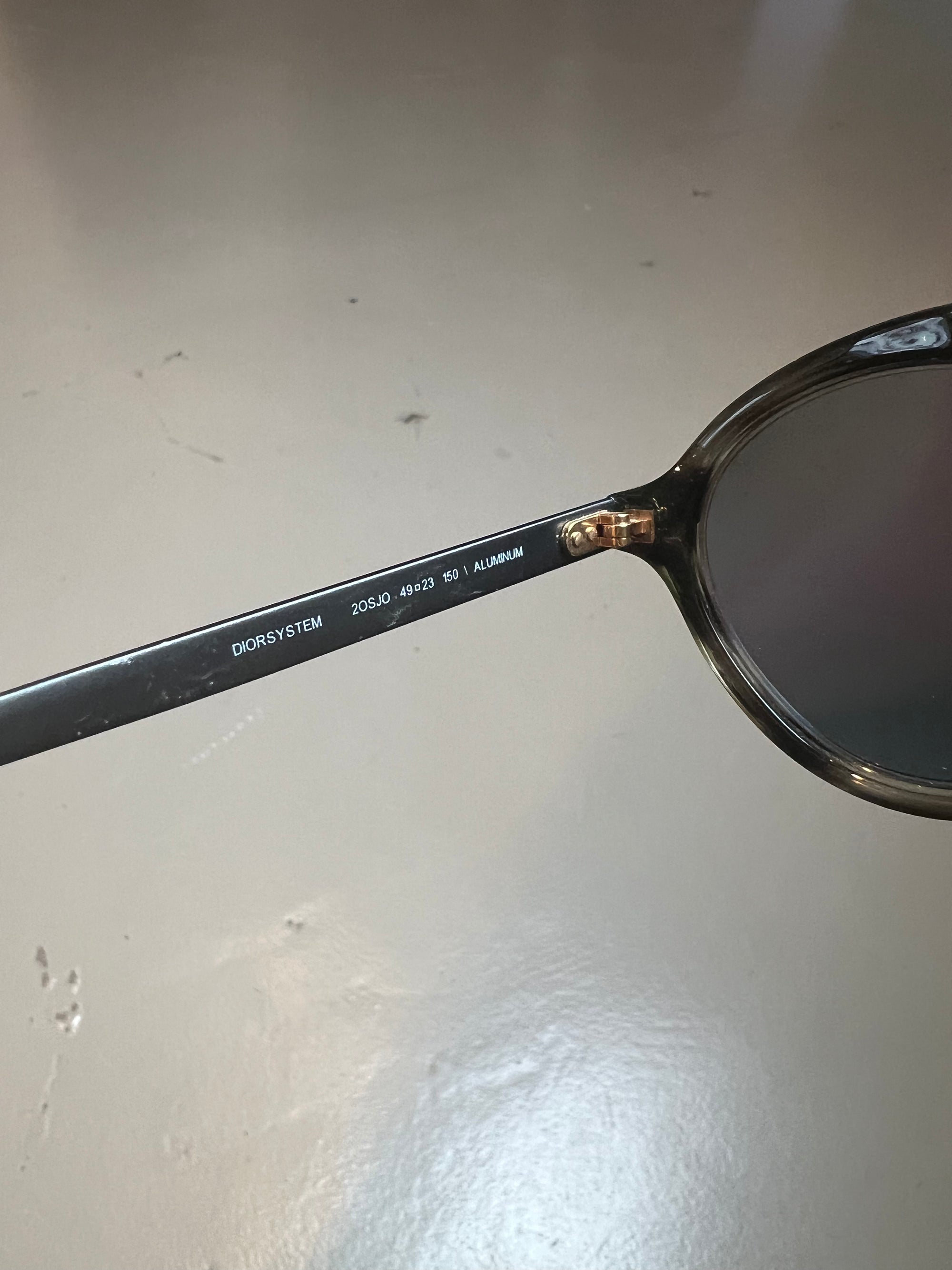 Detail-Produktbild einer Christian Dior Sonnenbrille vor grauem Hintergrund.