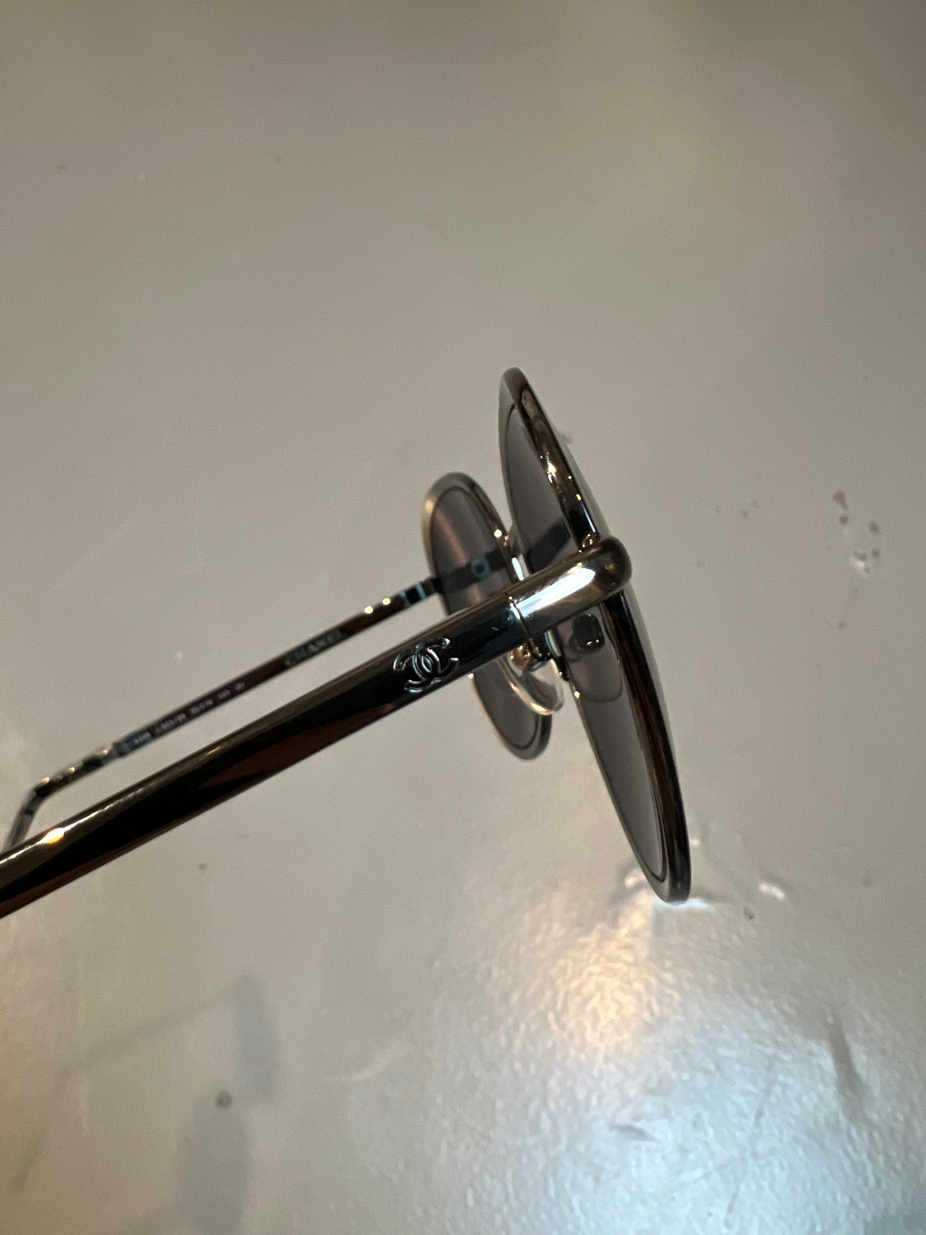Detail-Produktbild einer runden Chanel Sonnenbrille in schwarz vor grauem Hintergrund.